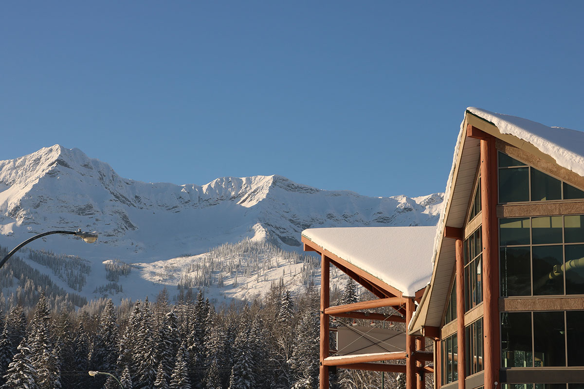 The snow covered triangular gabled roofs of the Stanford Fernie Resort stands in the foreground against the snow laden slopes and pine trees of the Rocky Mountains in BC.