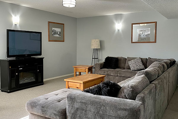A set of plates and cups and two decorative bottles sit on a four legged beige-brown wood stained side table placed against a grey wall in a suite at Stanford Fernie Resort in BC.