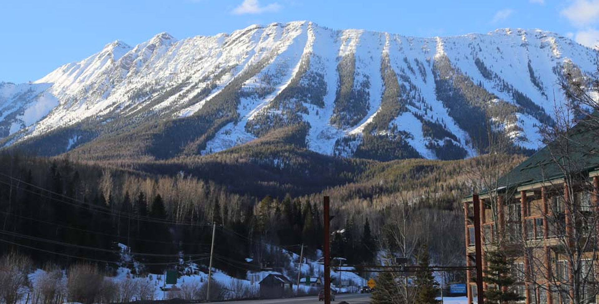 A partial view of the Stanford Fernie Resort set against the backdrop of thick arrays of conifer trees and the snow covered peaks of the Rocky Mountains in BC.