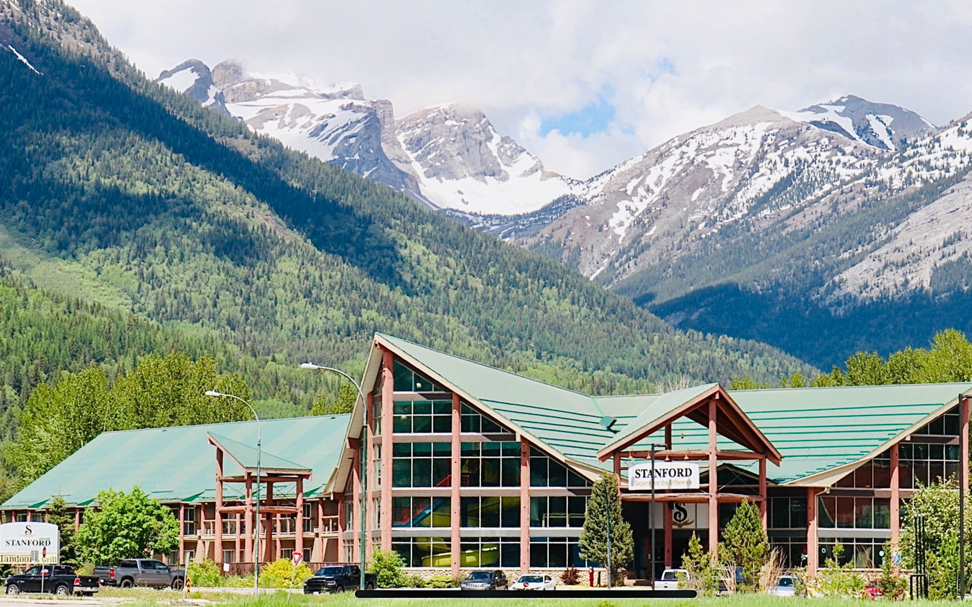 A profile view of the Stanford Fernie Resort building with its' triangular gable roof pointing skyward and floor to ceiling multi-level windows reflecting the bright blue skies in the summertime.