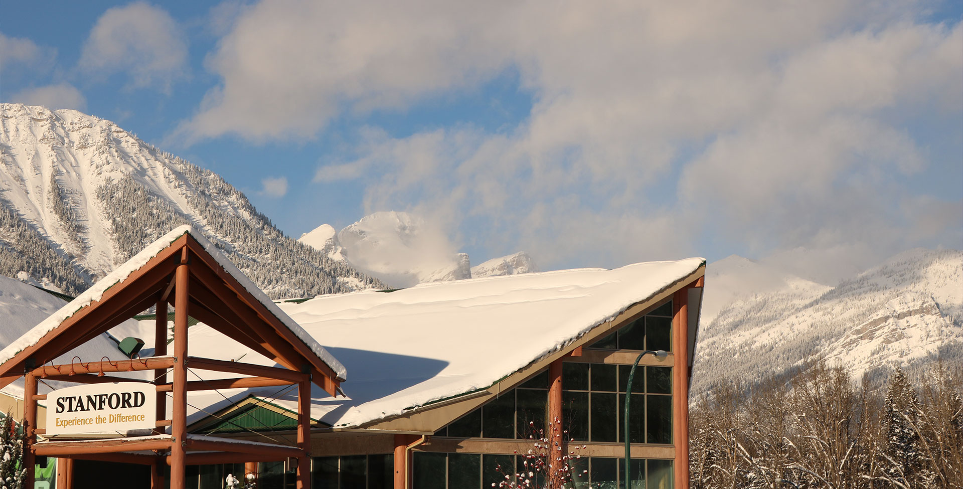 The snow-coated multi gabled rooftop of Stanford Fernie Resort stands in the foreground against the snow laden slopes and alpines trees of the Rocky Mountains on a bright sunny day.