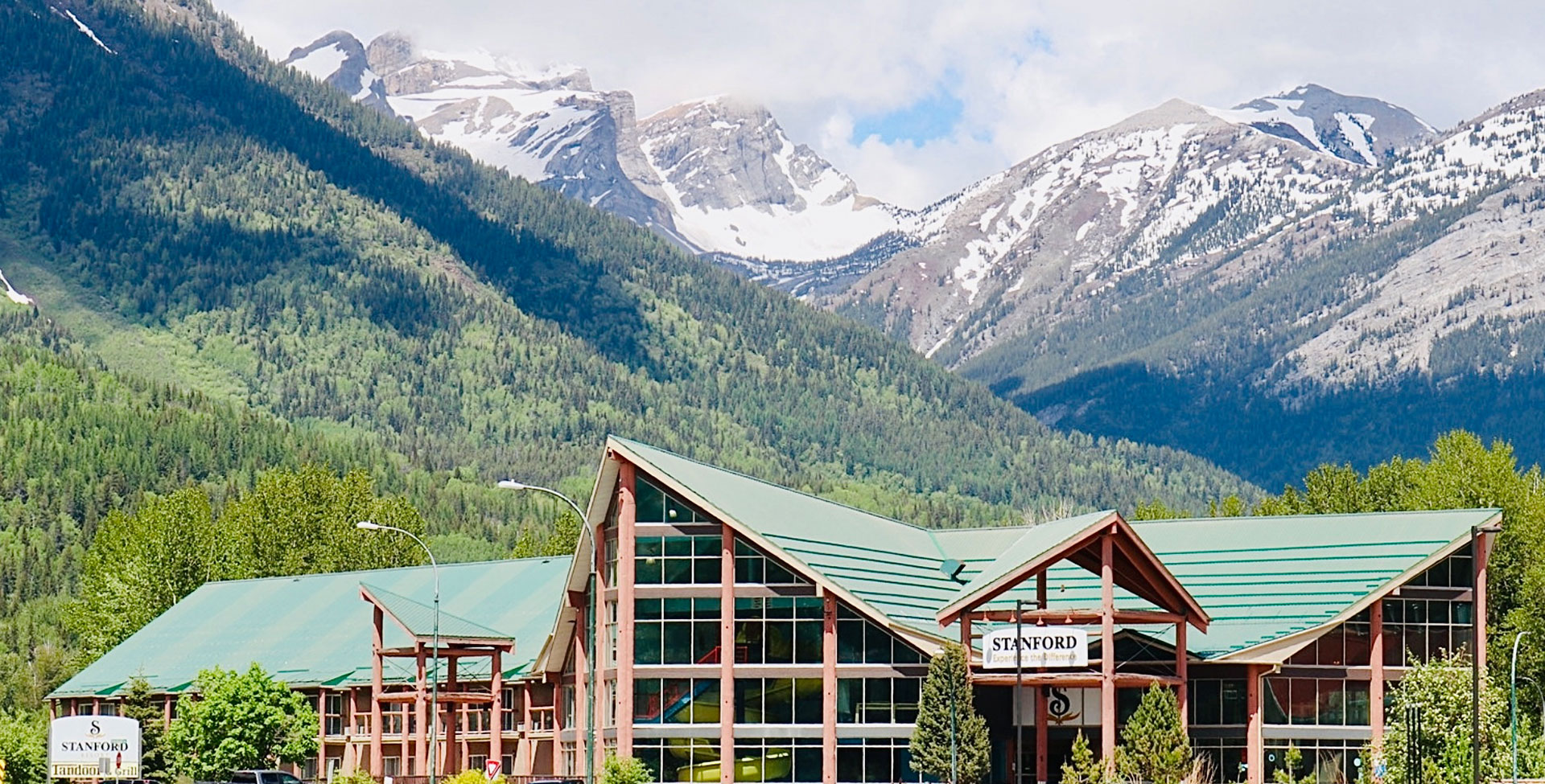 A skyward view of the triangular roof of the Stanford Fernie Resort building with ground to ceiling windows next to the triangular shaped roof portico bearing the company sign that greets visitors upon arrival.